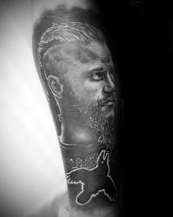 Detailed black-and-gray Ragnar Lothbrok tattoo with a bird silhouette on the forearm.