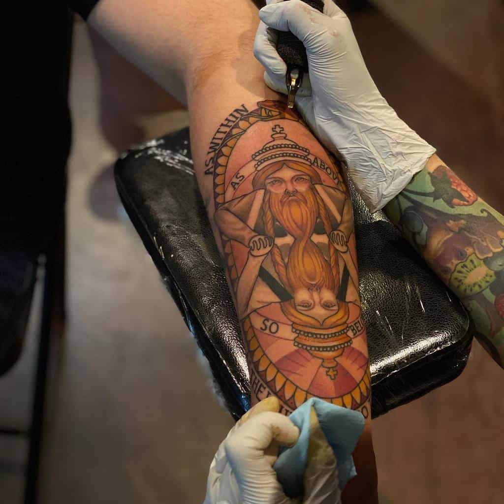 Detailed forearm tattoo featuring a mirrored bearded figure with 'As Above, So Below' text, designed in bold and warm tones