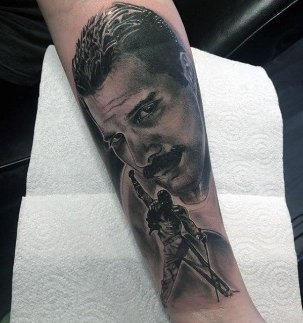 Freddie Mercury tattoo with a close-up portrait and a full-body silhouette in triumphant pose, done in black and grey realism.