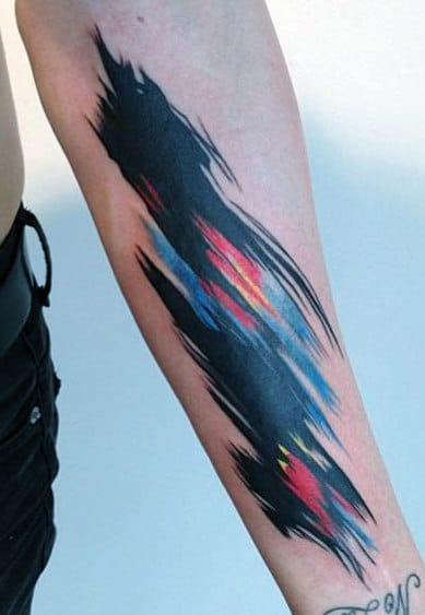 Abstract brushstroke tattoo with black, blue, red, and yellow on a person's forearm