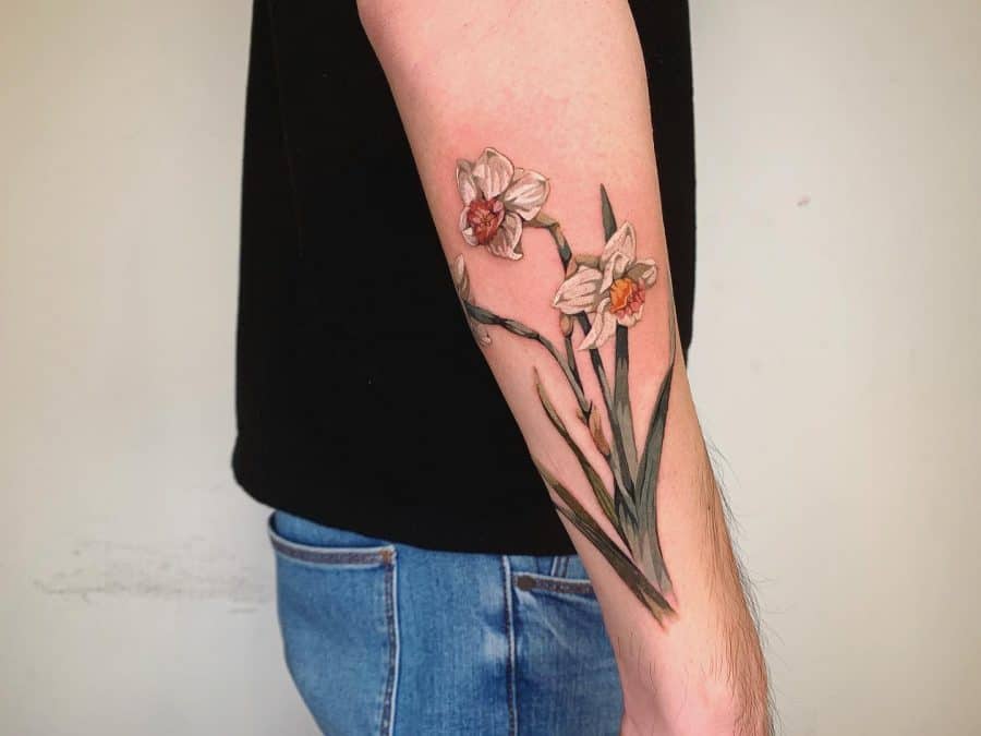 A beautifully detailed tattoo of two daffodils, showcasing realistic shading and subtle orange accents on the flowers, with long, delicate green leaves.