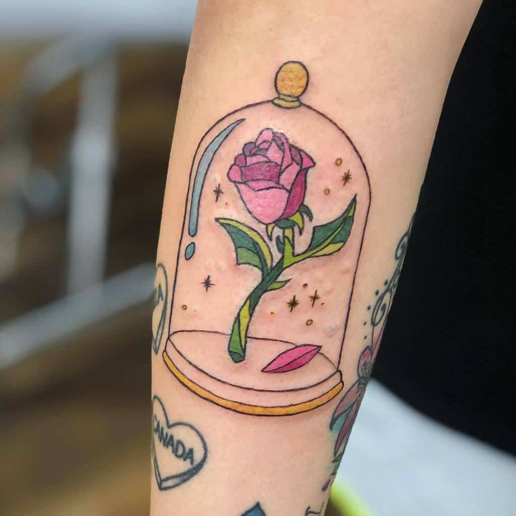 A colorful and whimsical tattoo of the Beauty and the Beast rose inside a glass dome, with stars and a falling petal, featuring soft pink and purple hues