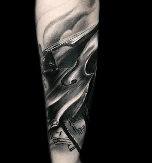Black and gray tattoo of a violin surrounded by flowing smoke and sheet music, blending realism and soft shading on the forearm.