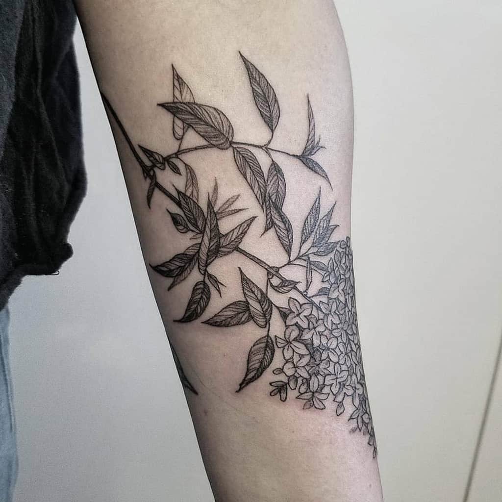 Black and grey tattoo of a lilac branch wrapping around the arm, featuring intricate fine-line details and delicate leaves.