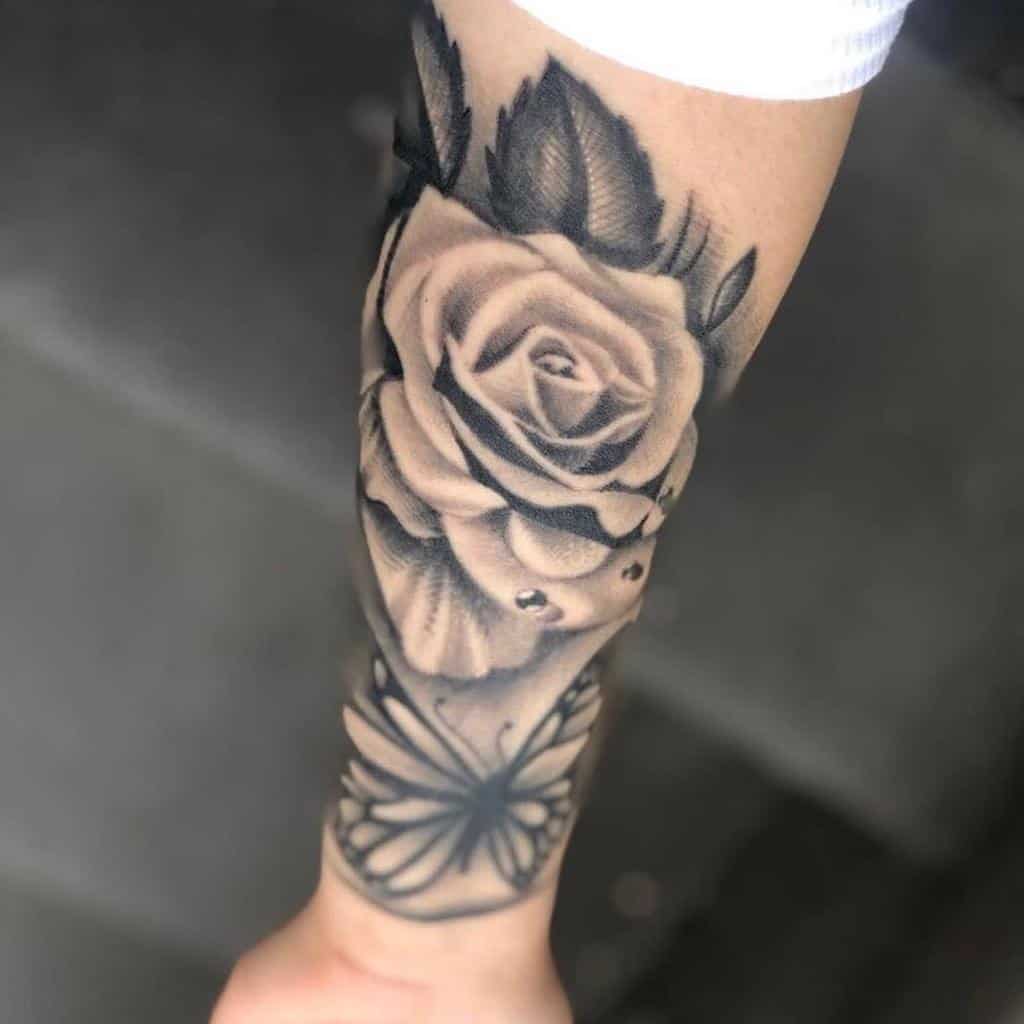 Black and grey rose tattoo on forearm with a butterfly beneath it