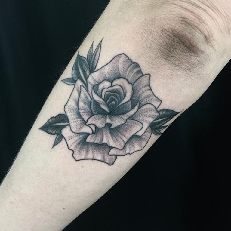A stunning black and gray rose tattoo blooms gracefully on the forearm, accompanied by intricately detailed leaves