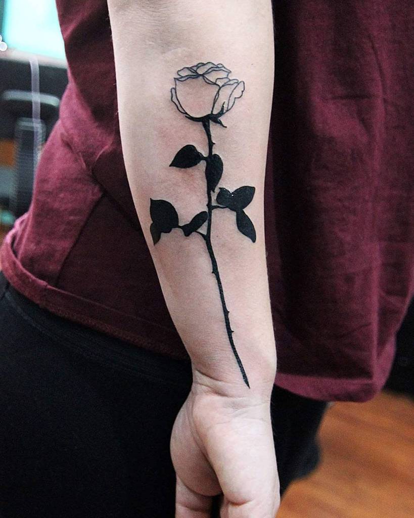 A beautifully intricate black rose tattoo adorns the forearm