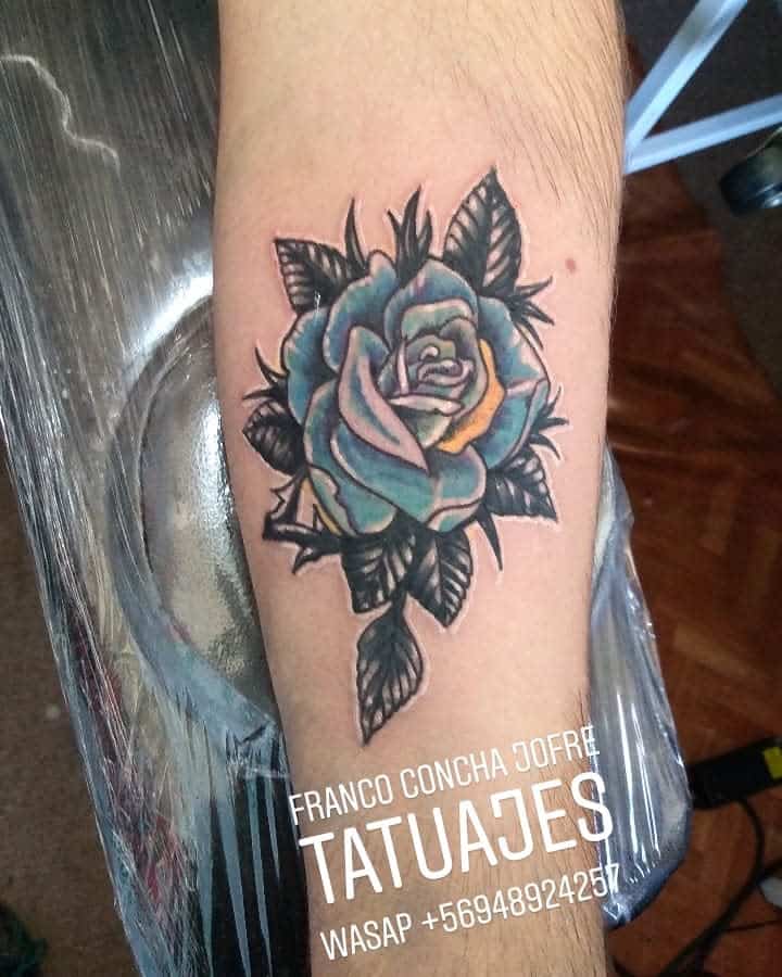 An exquisite arm tattoo featuring a vibrant blue rose entwined with lush leaves