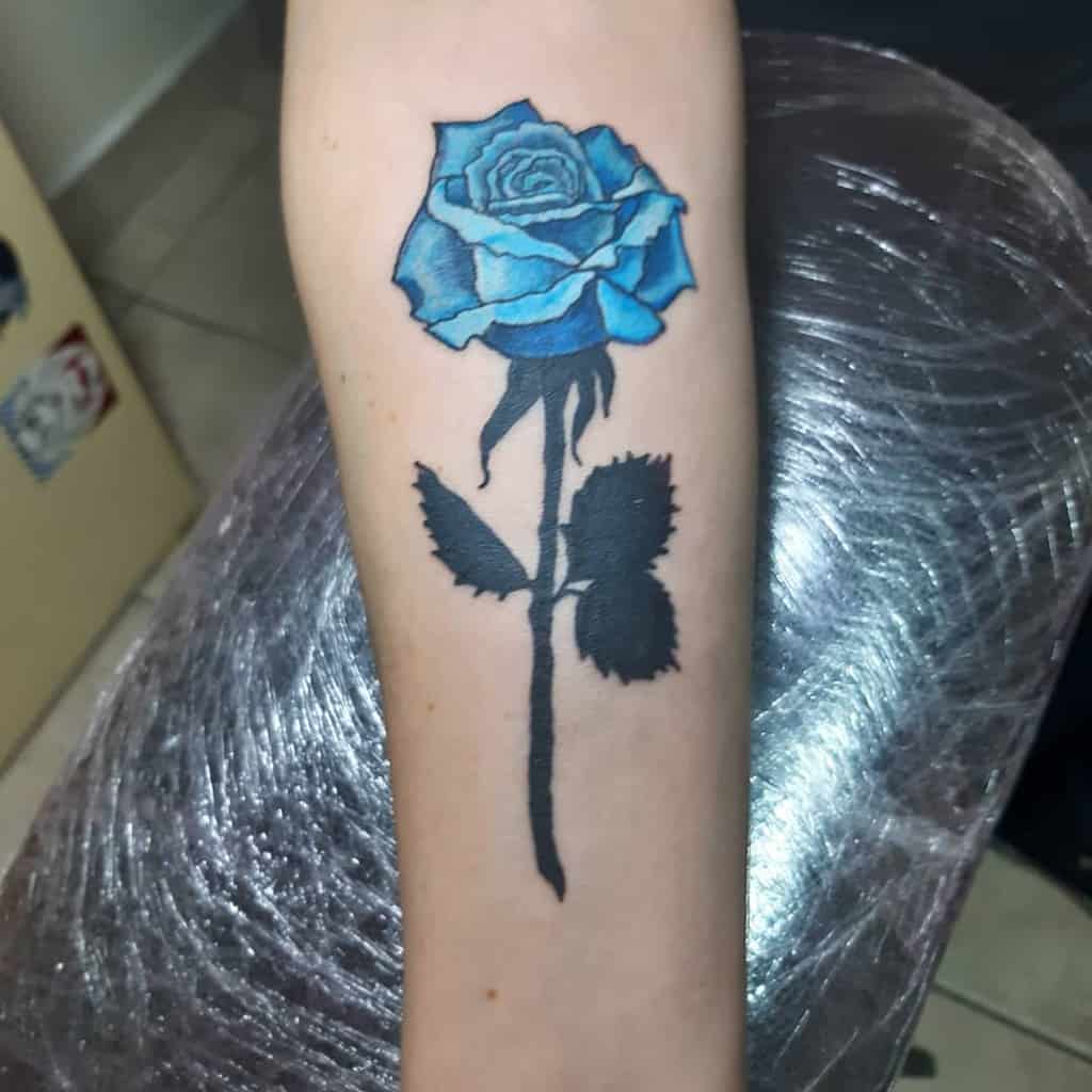 Blue rose tattoo on a forearm with black stem and leaves