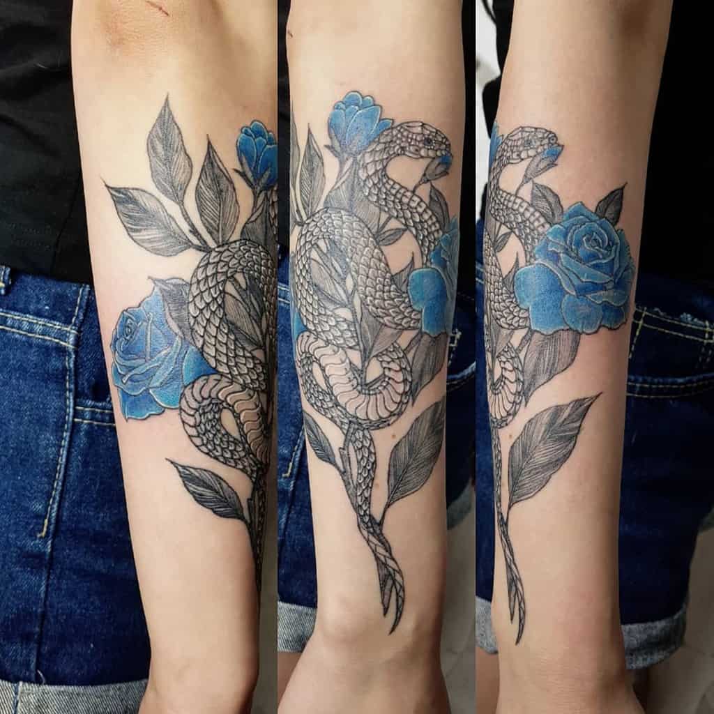 Snake with blue roses and leaves tattooed on a forearm