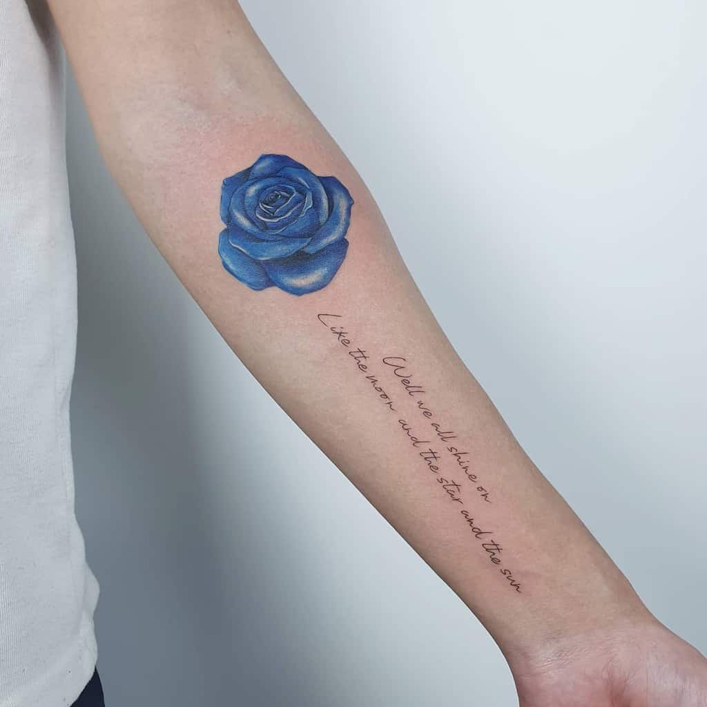 Forearm tattoo featuring a delicate blue rose, elegantly complemented by cursive text beneath on light skin