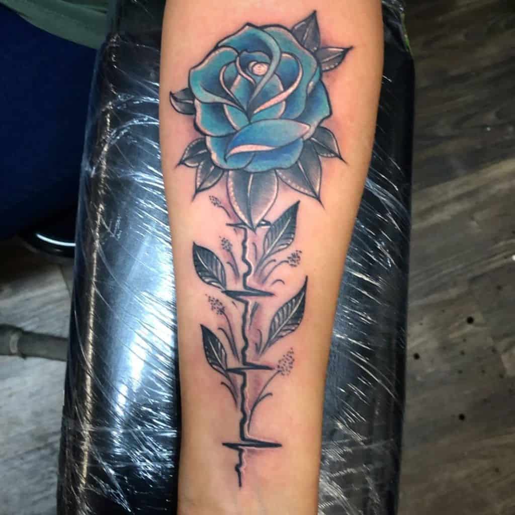 A beautiful tattoo of a blue rose elegantly adorns the arm, its vibrant hues complemented by intricately detailed thorns and lush leaves