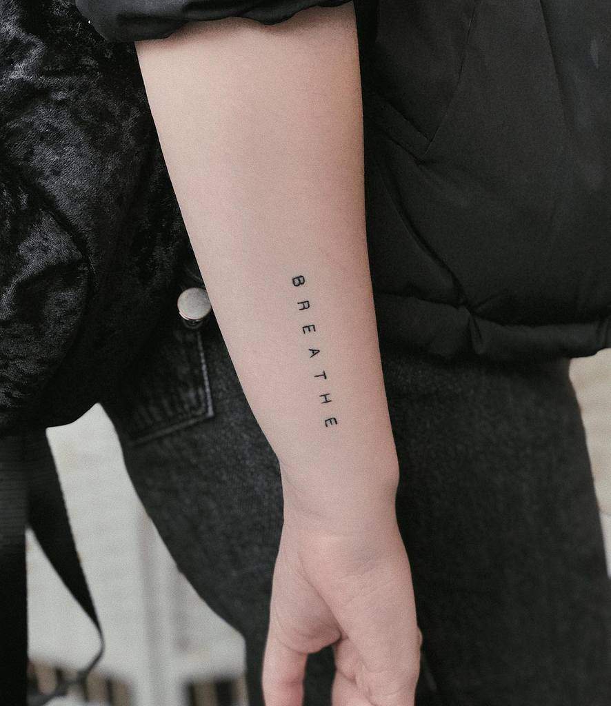 Forearm tattoo featuring the word "BREATHE" in a sleek, vertical black font