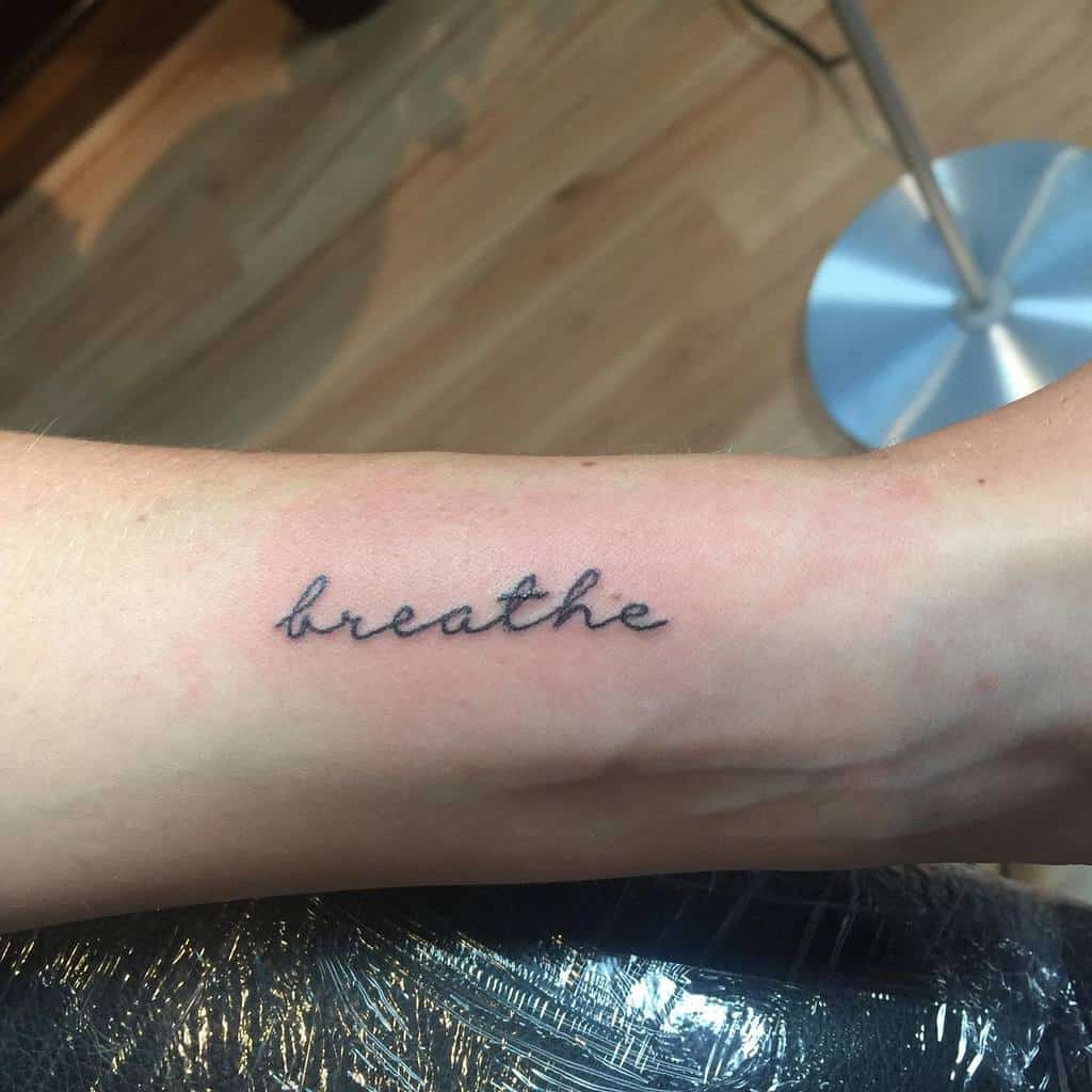 A delicate script tattoo graces a person's forearm, elegantly capturing the word "breathe"