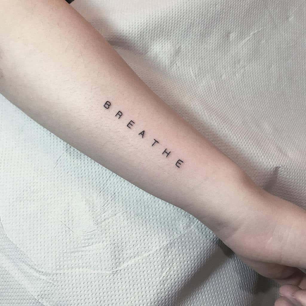 On the forearm, a simple black font spells out "BREATHE," serving as a gentle reminder to find calm amidst chaos