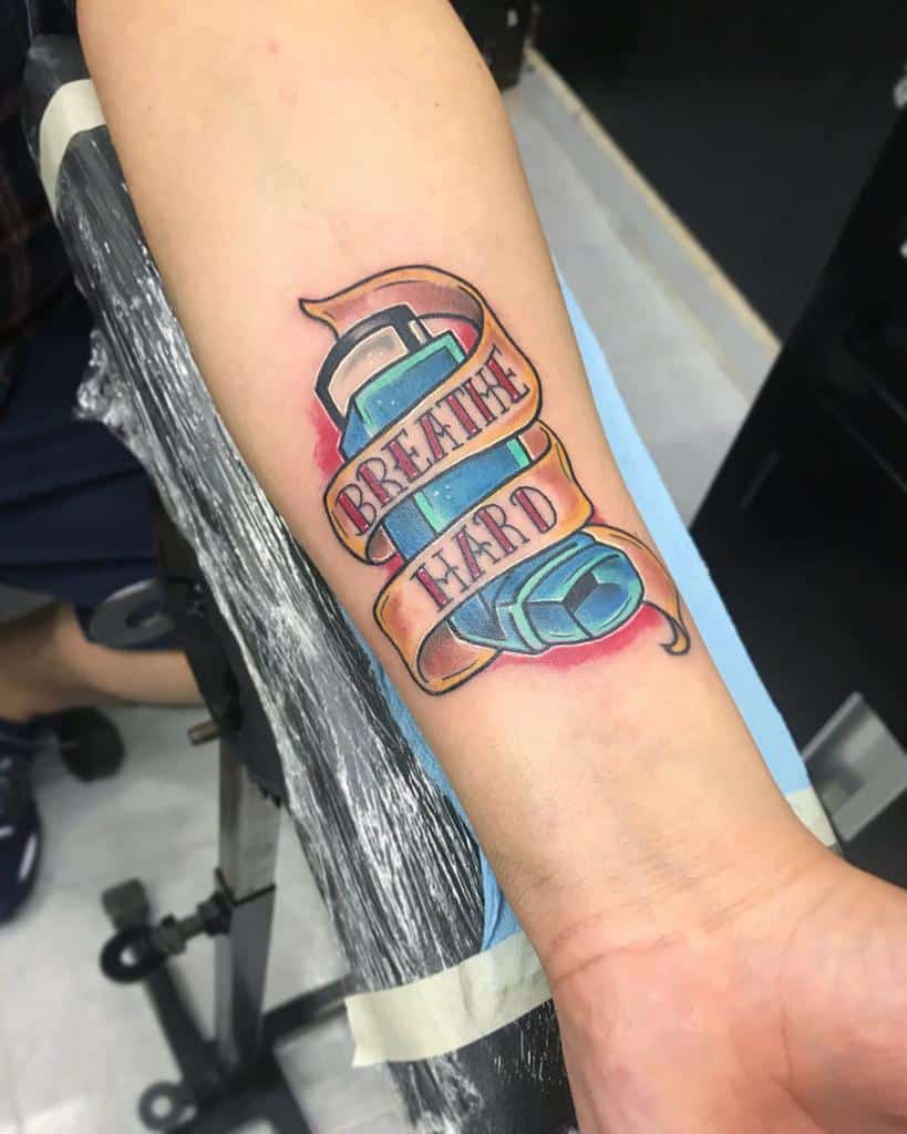 Colorful forearm tattoo of an inhaler wrapped with a banner that reads 'Breathe Hard,' symbolizing respiratory strength