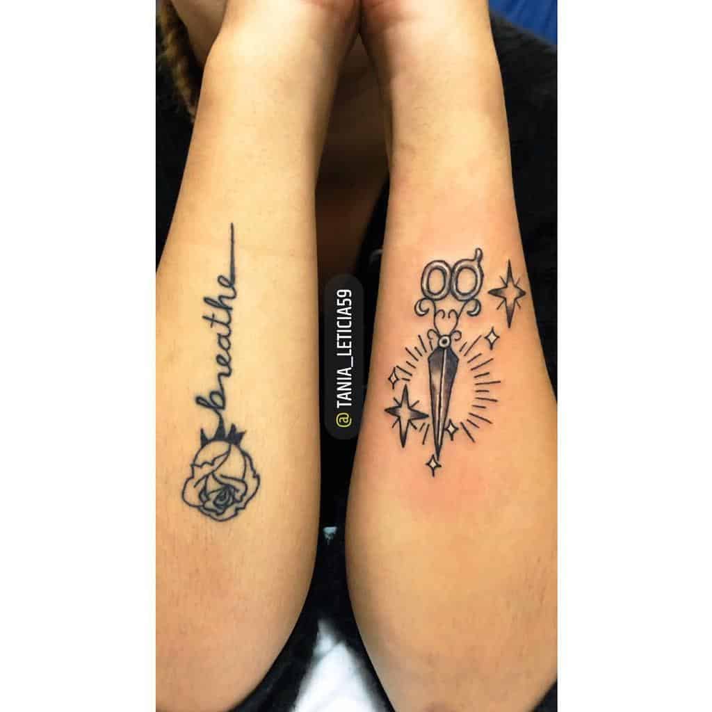 Two forearm tattoos: a blooming rose intertwined with the word "breathe" and a pair of scissors adorned with a heart and twinkling stars