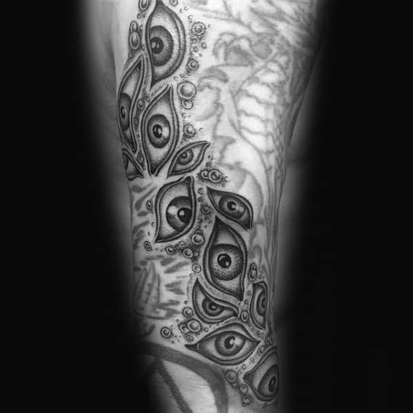 Black and grey tattoo of multiple eyes surrounded by intricate bubble details, creating an eerie and surreal pattern that flows along the arm.