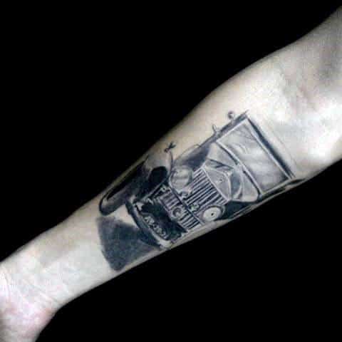 Forearm tattoo of a vintage car in black and grey design, three-quarter front perspective