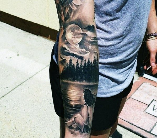 Tattoo on arm shows a woman by a lake with a forest and moon in the background