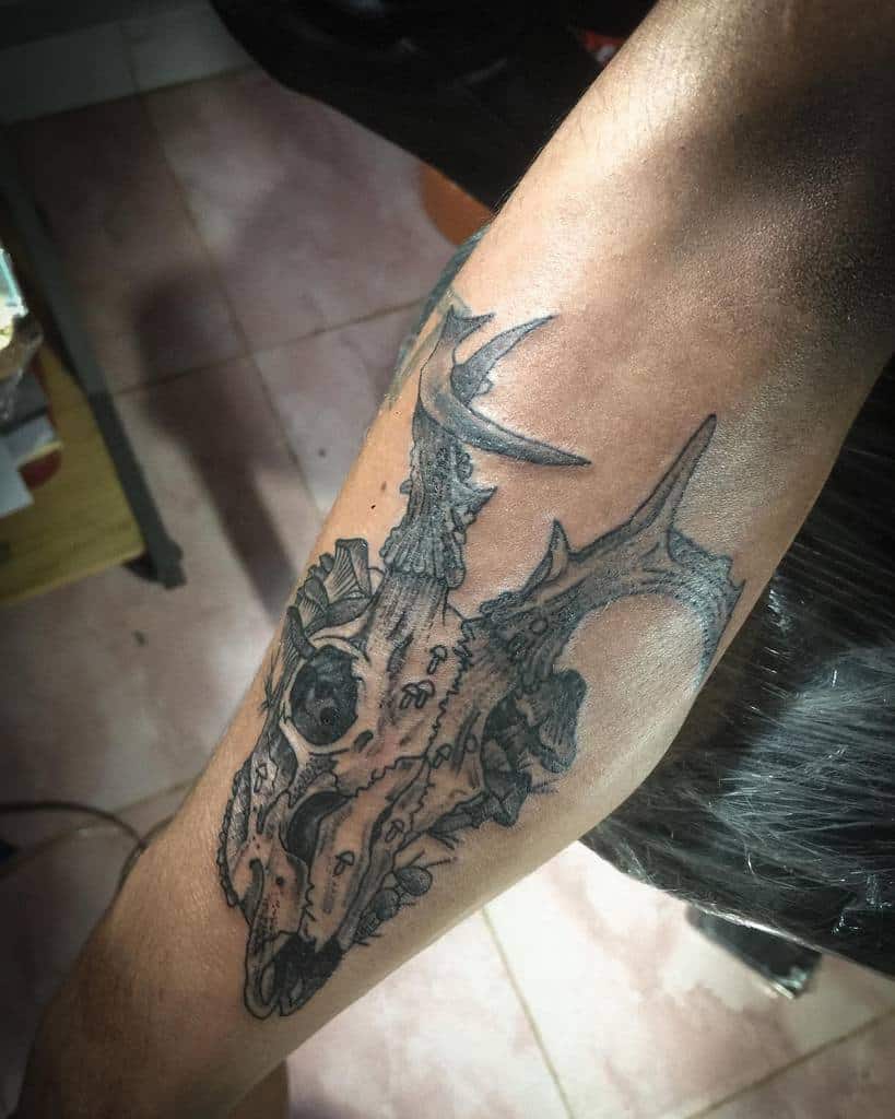 A detailed tattoo of a deer skull with antlers adorns a person's forearm