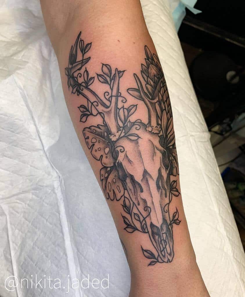 Arm tattoo of a majestic deer skull with branches and leaves intertwined