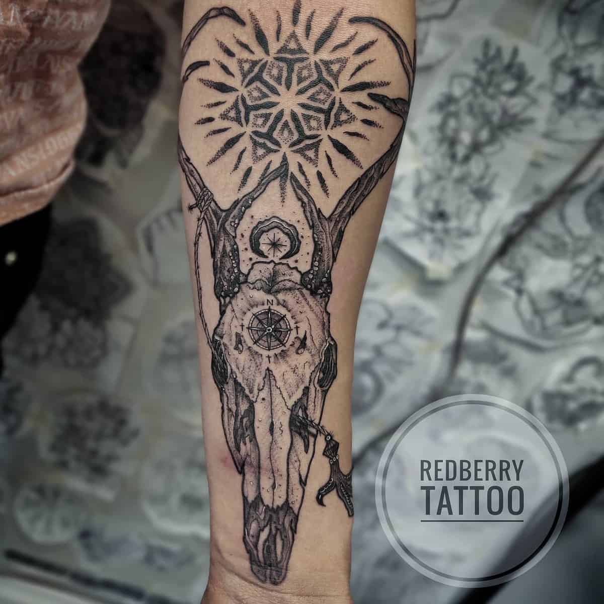 Forearm tattoo featuring a deer skull with intricate geometric patterns and a compass