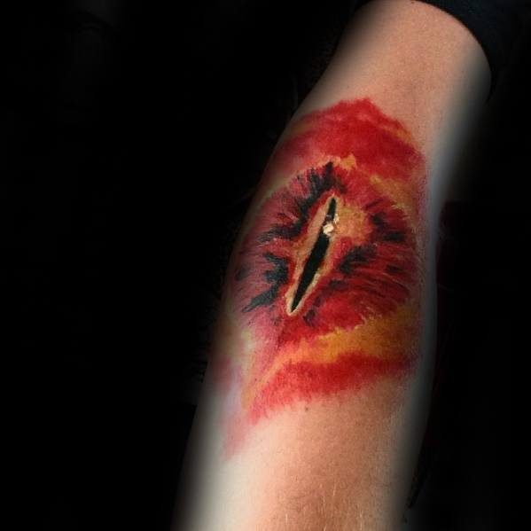 A striking tattoo of a fiery, eye-like design reminiscent of the Eye of Sauron adorns a person's forearm against a dark background