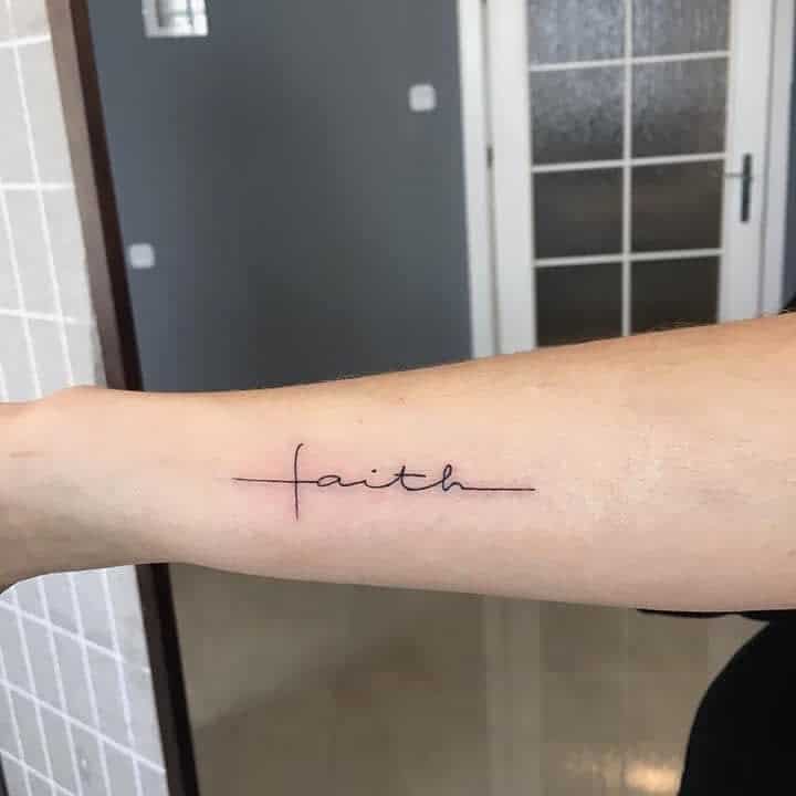 A graceful tattoo of the word "faith" in elegant cursive perfectly aligns with a cross, adorning the forearm