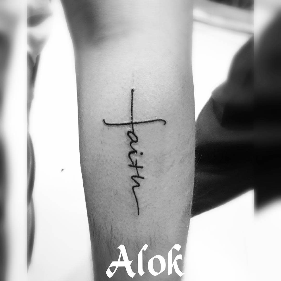 A black tattoo of "faith" in elegant cursive adorns the forearm, seamlessly incorporating a delicate cross for added symbolism