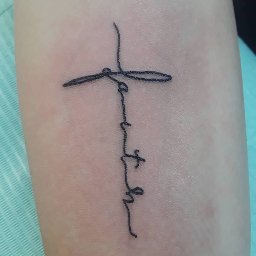 Minimalist tattoo of a cross elegantly intertwined with the word "faith" on the forearm
