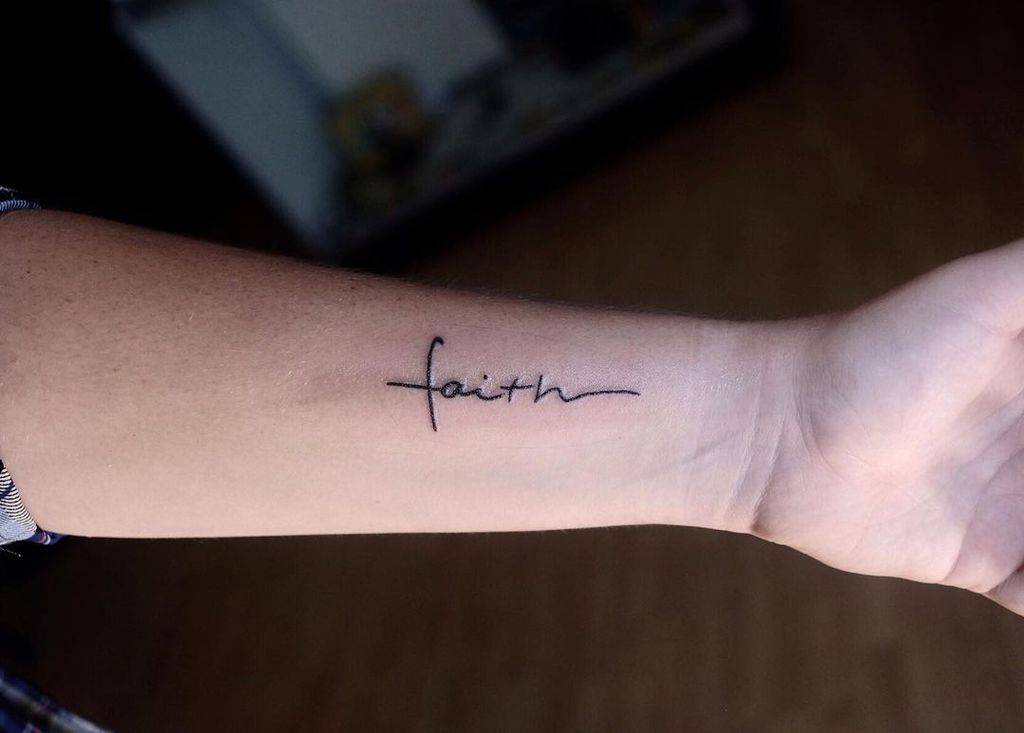 A forearm tattoo elegantly intertwines the word "faith" with a beautifully crafted cross, symbolizing strength and belief