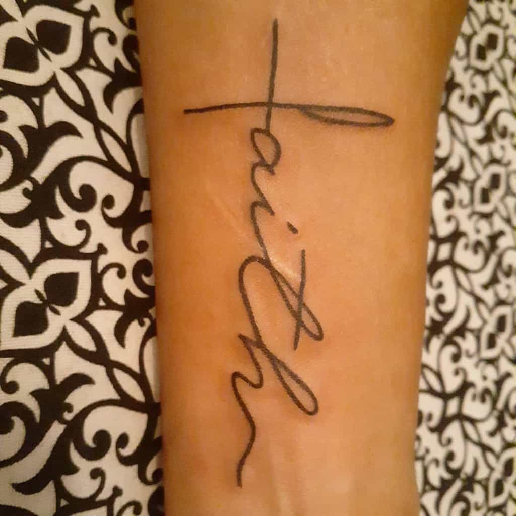 Tattoo of the word "faith" written vertically alongside a delicate cross on forearm