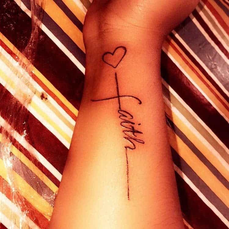 Tattoo of the word "faith" elegantly intertwined with a cross and heart on a person's arm