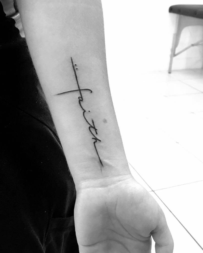 A tattoo of the word "faith" in elegant cursive, complemented by a delicate cross, adorns a person's forearm