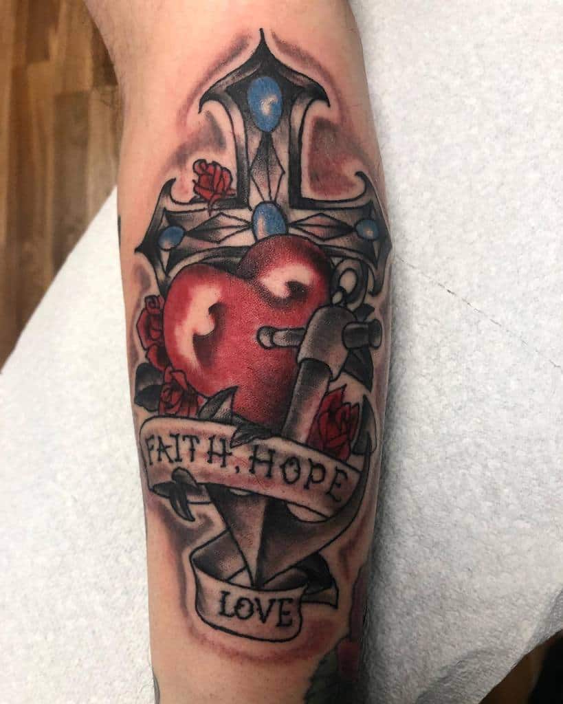 Tattoo of a heart pierced by a sword, entwined with a banner elegantly reading "Faith, Hope, Love," beautifully decorated with roses