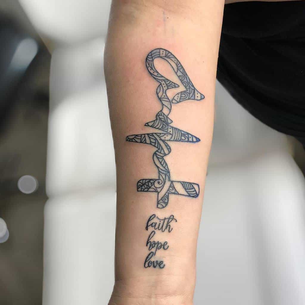 A forearm tattoo with a stylized, intricate design of the words 'Faith Hope Love,' featuring a bold, patterned cross and heartbeat line intertwined