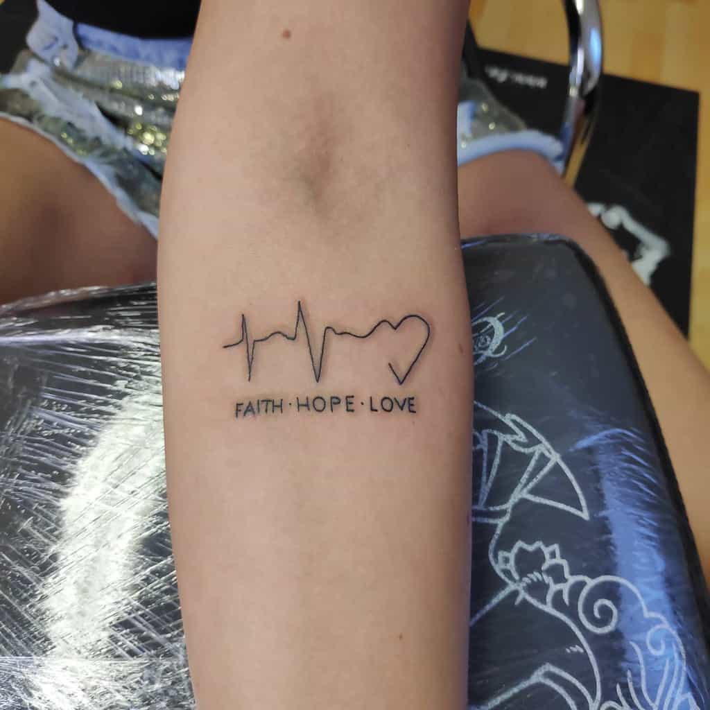 A simple forearm tattoo featuring the words 'Faith Hope Love' below a minimalist heartbeat line ending in a heart symbol