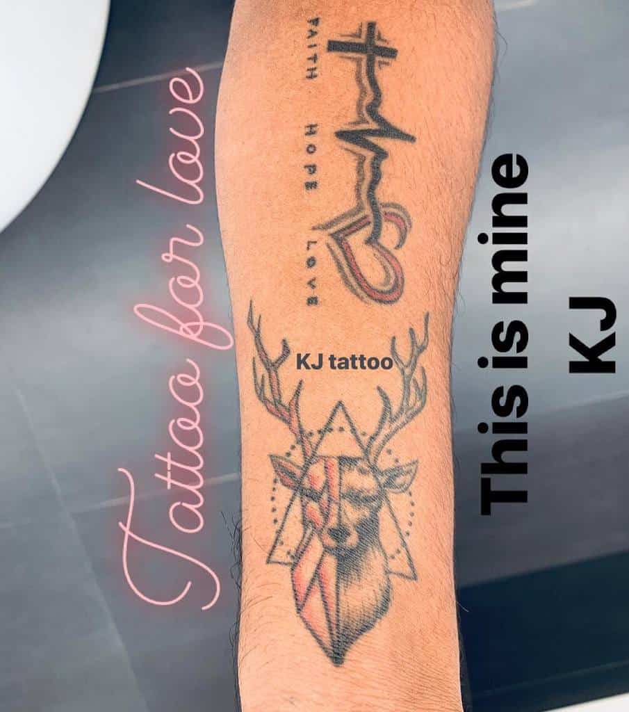 A forearm tattoo that features 'Faith Hope Love' vertically aligned with a heartbeat line and heart symbol, alongside a geometric deer design with antlers and a triangle pattern
