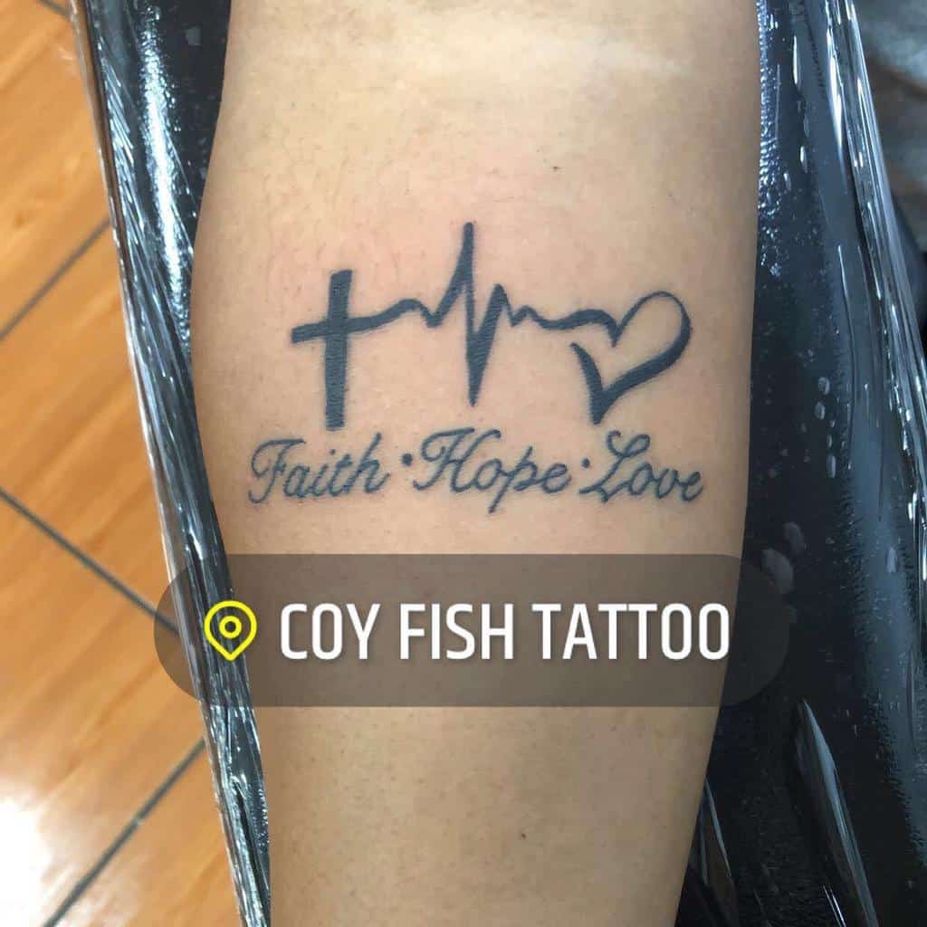 A forearm tattoo that displays the words 'Faith Hope Love' in cursive below a cross, heartbeat line, and heart symbol, with the text 'Coy Fish Tattoo' overlayed on the image