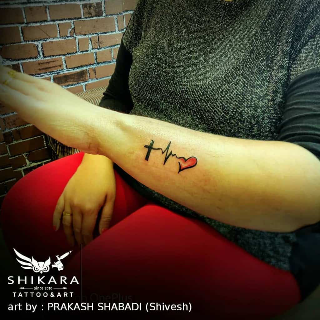 Forearm tattoo of a cross, heartbeat line, and heart symbolizing faith, hope and love