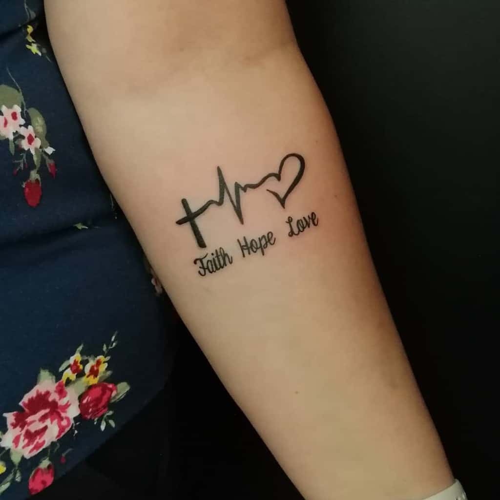 A forearm tattoo featuring a cross, a heartbeat line, and a heart symbol, followed by the words 'Faith Hope Love' in cursive script