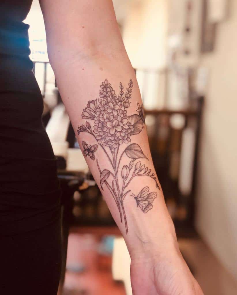 Elegant black and grey forearm tattoo of a lilac branch with delicate butterflies, featuring fine-line details and soft shading.