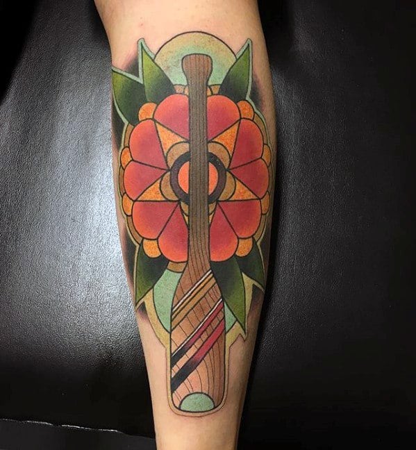 Alt text: Colorful tattoo of a canoe paddle surrounded by vibrant floral elements, combining bold shapes and striking colors in a unique design.
