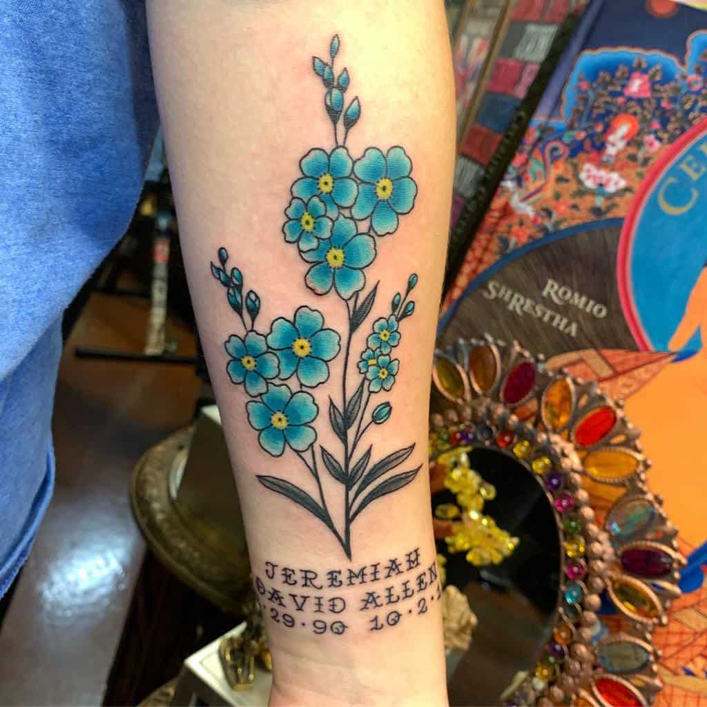 Forget-me-not flowers with vibrant blue petals and a meaningful tribute to "Jeremiah David Allen" on the forearm