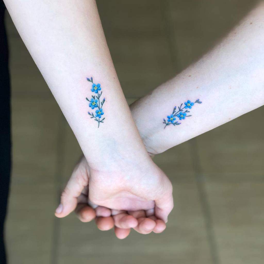 A pair of delicate forget-me-not tattoos on each forearm, with soft blue flowers and slender stems, beautifully placed on opposite arms