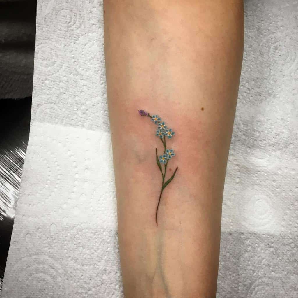 A delicate forget-me-not tattoo graces the person's forearm, its blue petals capturing timeless elegance