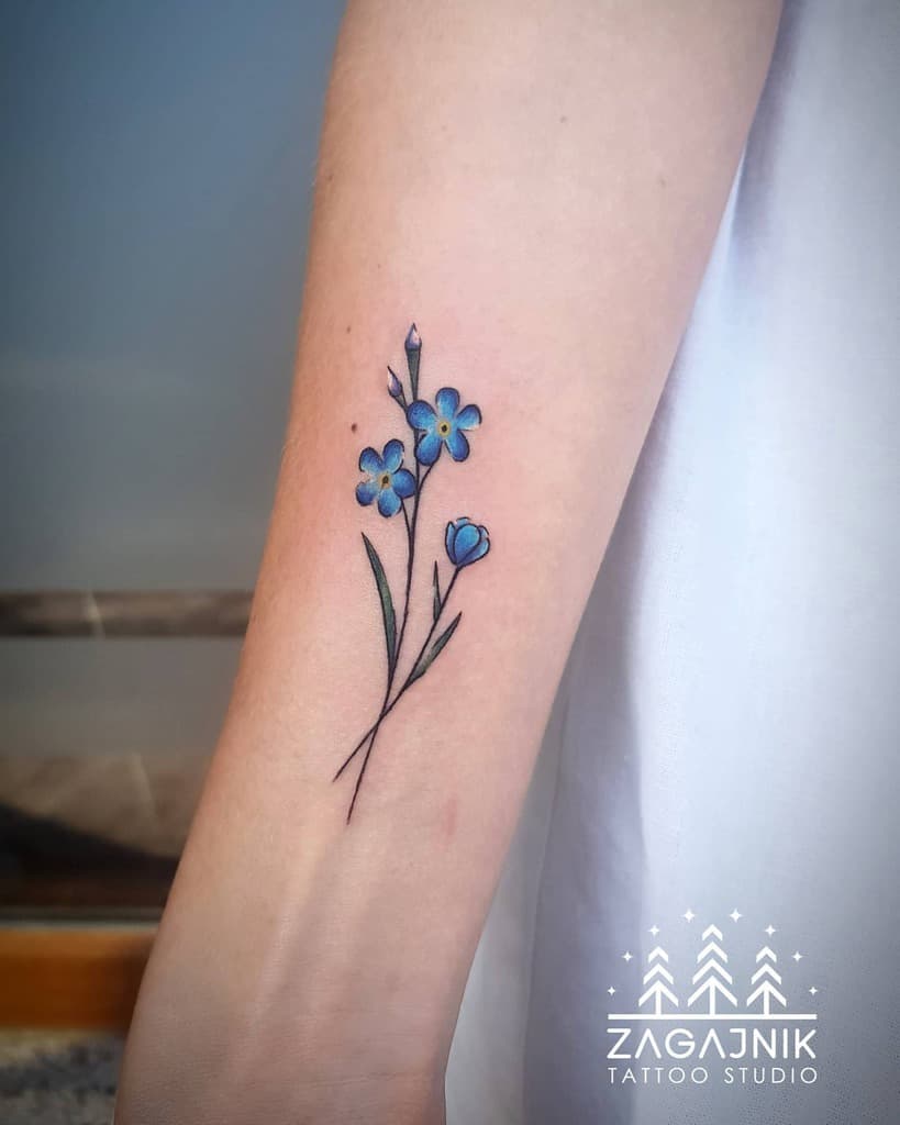 A tattoo of delicate forget-me-not blue flowers with lush green stems graces the forearm