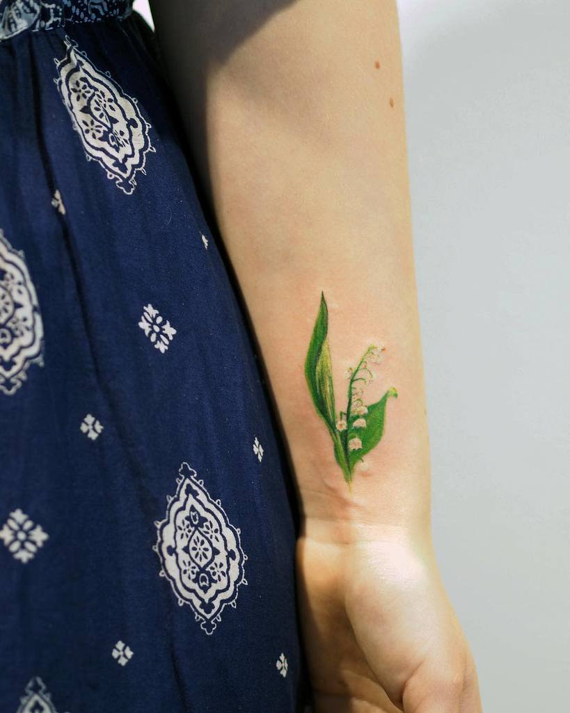 Delicate watercolor Lily of the Valley tattoo, featuring soft green leaves and tiny white bell-shaped flowers in a realistic style