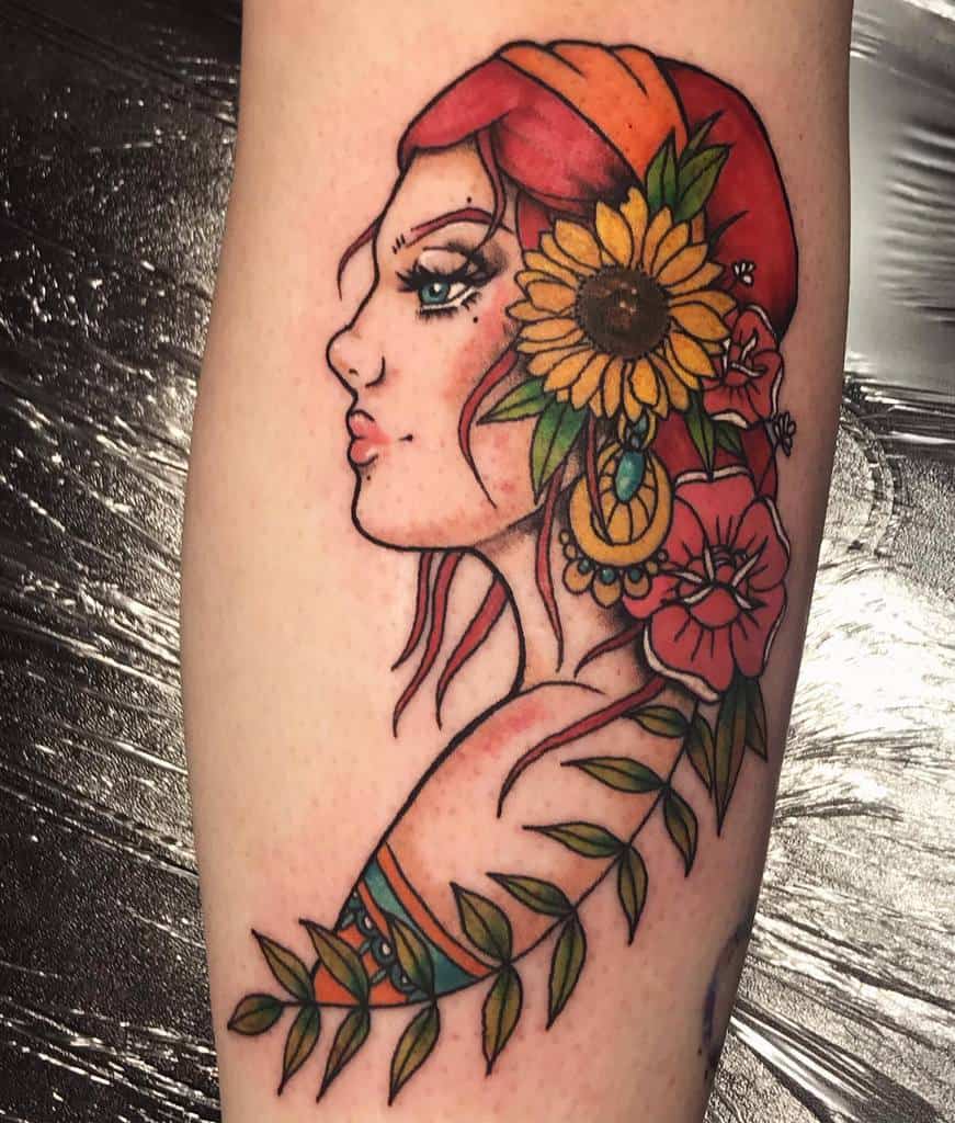 A colorful tattoo of a gypsy woman with red hair, a sunflower, and flowers in her hair, with vines extending down the forearm